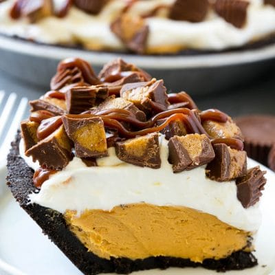 A slice of chocolate peanut butter pie topped with whipped cream, chocolate sauce and peanut butter cups.