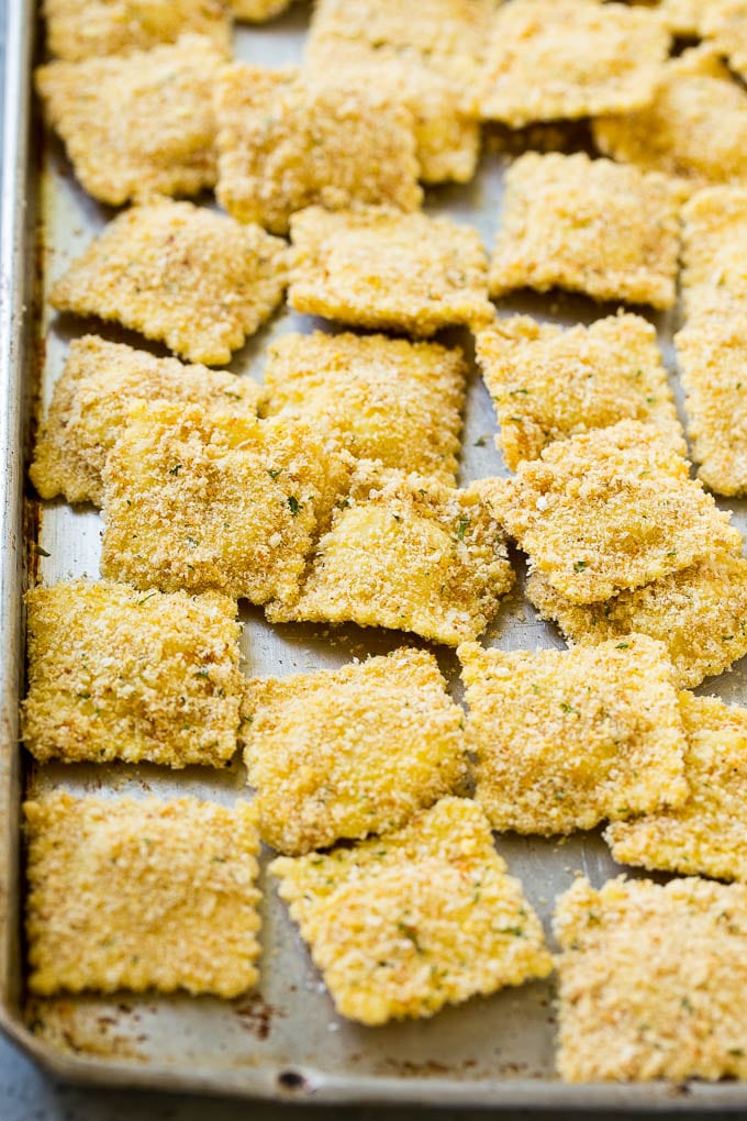 Breaded ravioli on a sheet pan ready to be fried.