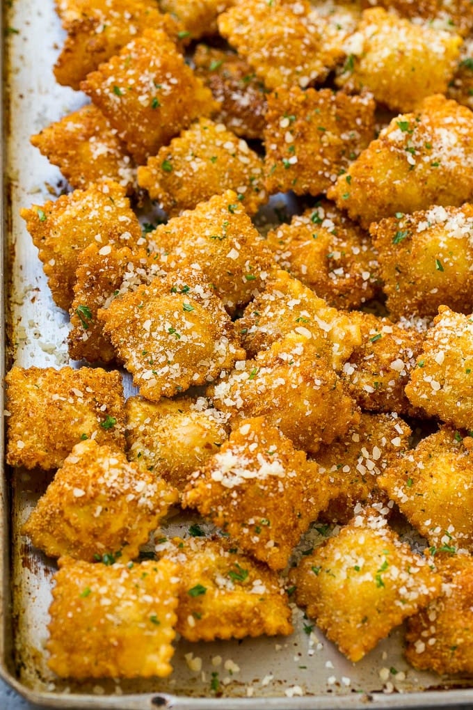 A sheet pan full of fried ravioli topped with parmesan cheese.