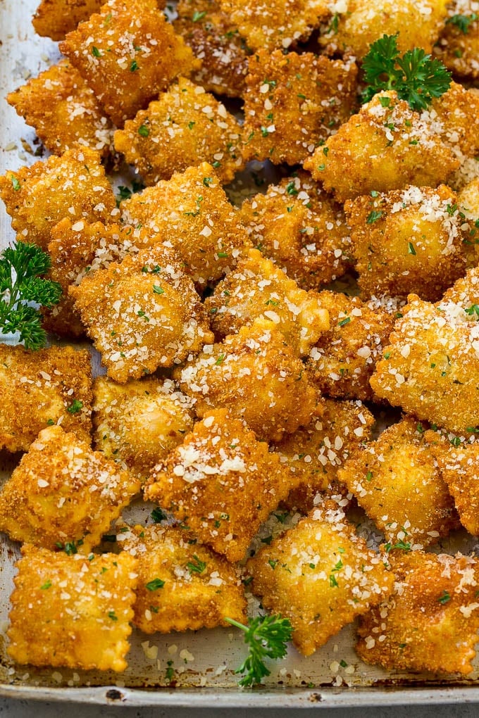 A pile of fried ravioli topped with parmesan cheese and chopped parsley.