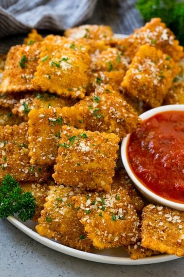 A plate of fried ravioli topped with parmesan and parsley, and served with a side of marinara sauce.