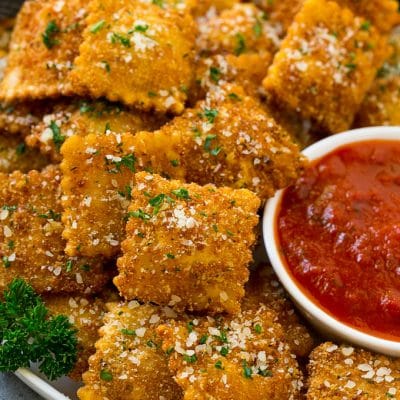 A plate of fried ravioli topped with parmesan and parsley, and served with a side of marinara sauce.