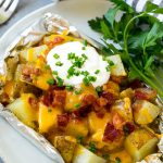 Grilled potatoes in foil that are cooked in ranch butter then topped with cheddar cheese, bacon and sour cream.