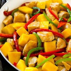 Mango chicken in a skillet with red and green sliced peppers.