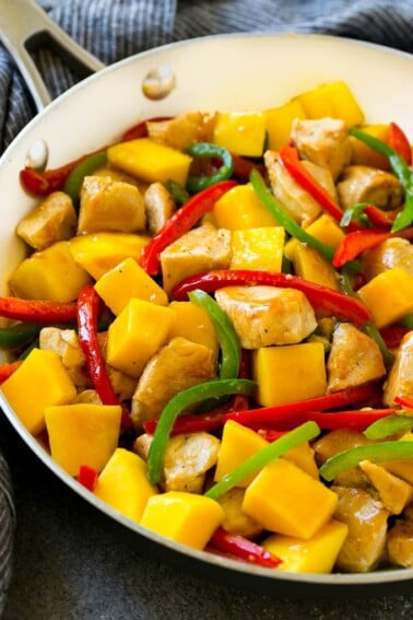 Mango chicken in a skillet with red and green sliced peppers.
