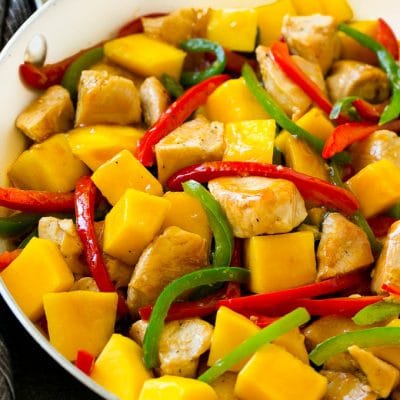 Mango chicken in a skillet with red and green sliced peppers.