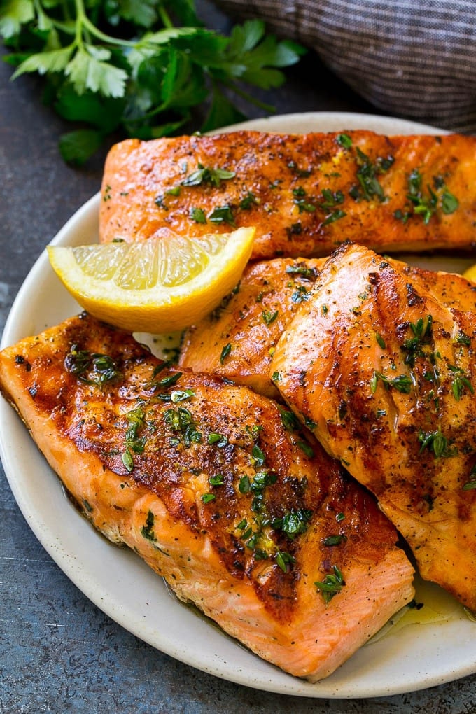 A platter of marinated salmon fillets that are grilled and topped with fresh herbs.