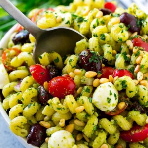 Pesto pasta salad with cherry tomatoes, olives, mozzarella balls, pine nuts and red onion.
