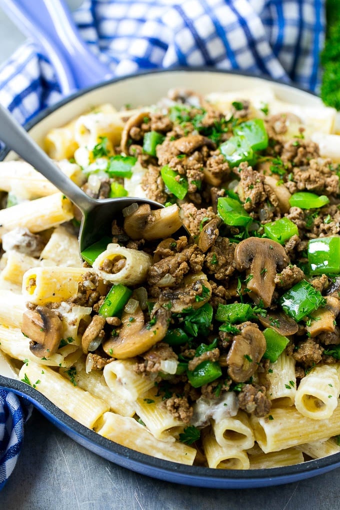 A pan of philly cheesesteak pasta with a serving spoon in it.