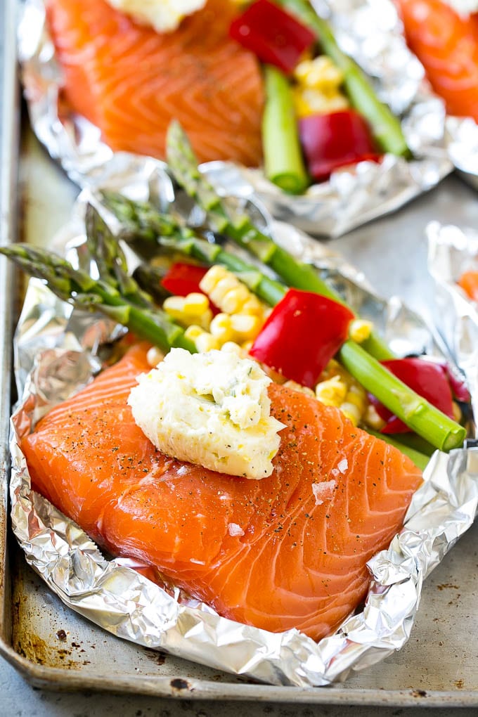 A salmon fillet topped with seasoned butter in a foil packet with vegetables.