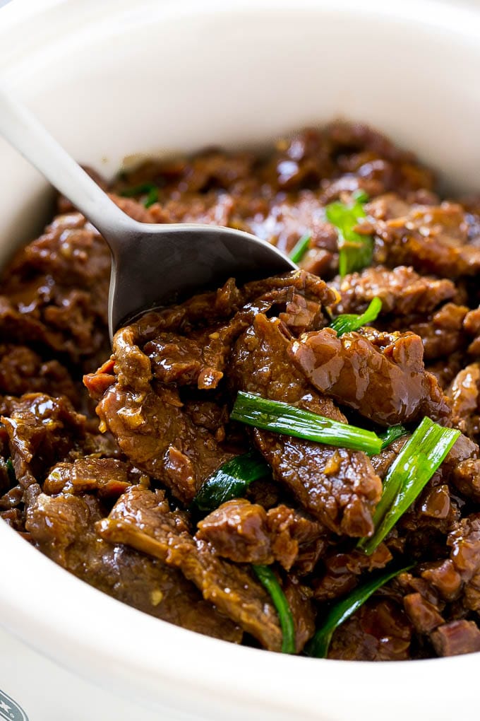 A slow cooker full of Mongolian beef in a savory sauce with green onions.