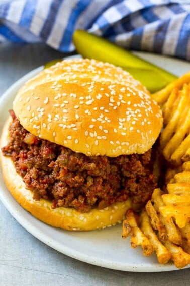 Slow cooker sloppy joe on a bun served with fries and pickles.