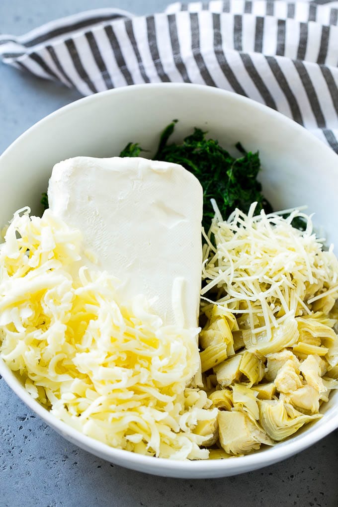 Cream cheese, spinach, artichokes and shredded cheese in a bowl.