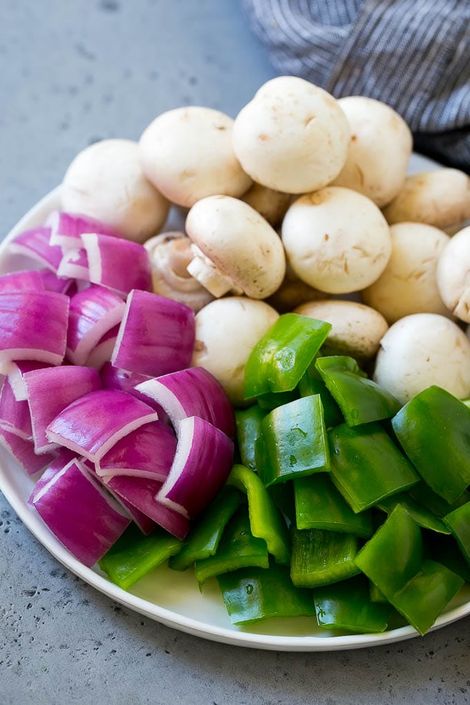 A plate of mushrooms, cut up bell peppers and red onion pieces.