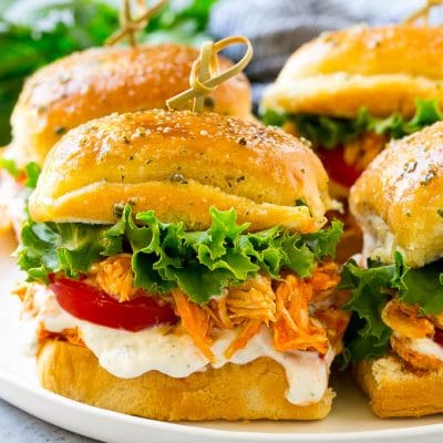 A plate of buffalo chicken sliders layered with lettuce, tomato and ranch.