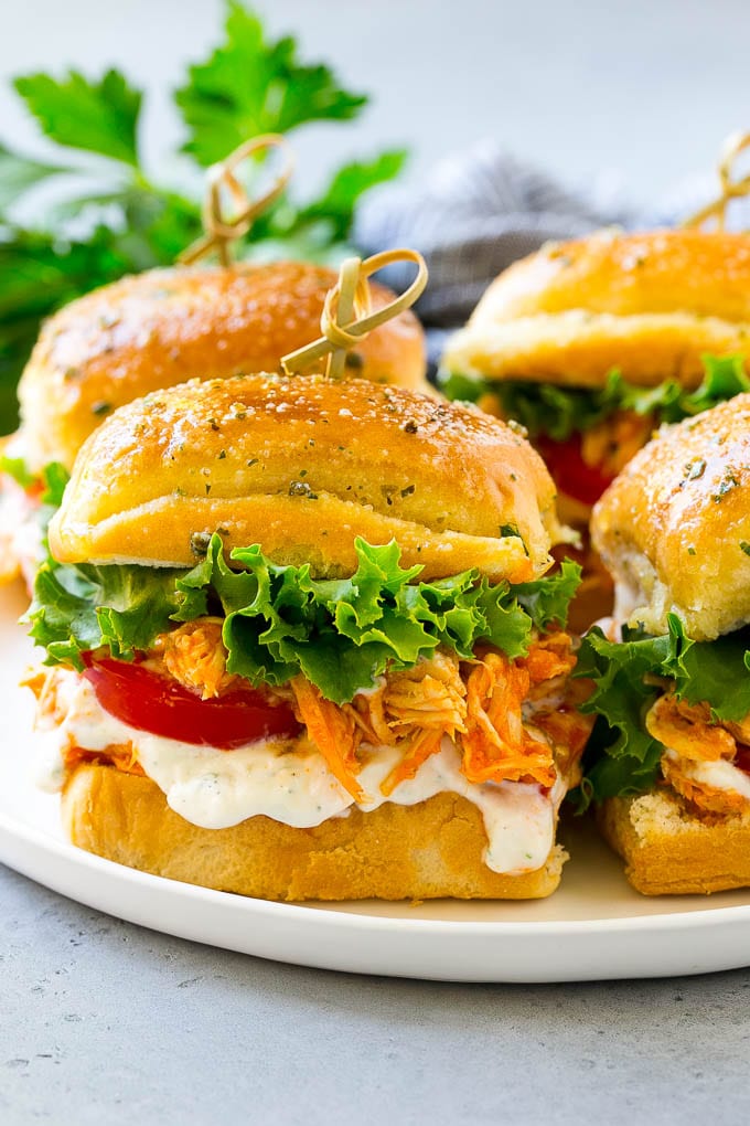 A plate of buffalo chicken sliders layered with lettuce, tomato and ranch.