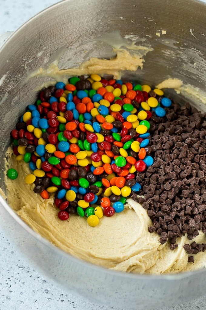 Cookie dough in a mixing bowl with chocolate chips and M&M's.