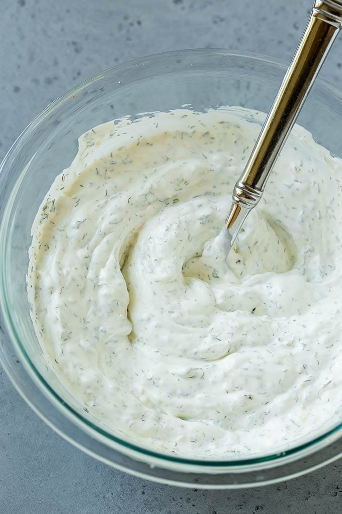 A mixing bowl full of dill dip with a spoon.