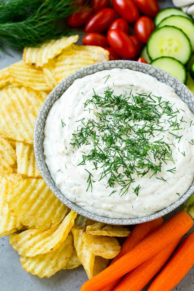 A bowl of creamy dill dip served with potato chips and vegetables.