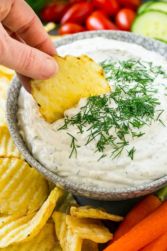 A bowl of dill dip with a chip scooping into it.