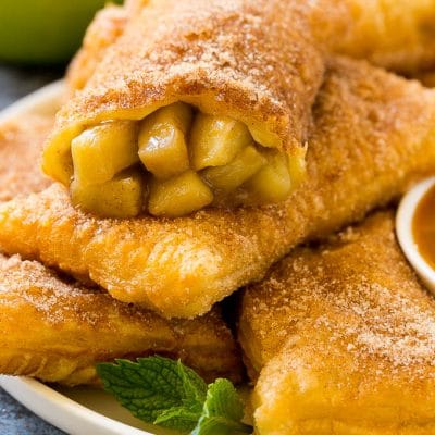 Fried apple pies on a plate served with caramel sauce and topped with cinnamon sugar.