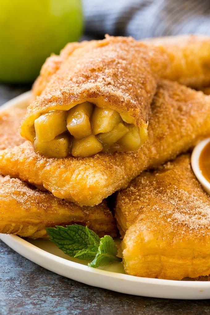 Fried apple pies on a plate served with caramel sauce and topped with cinnamon sugar.