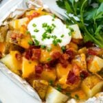 Grilled potatoes in foil on a serving plate garnished with herbs.