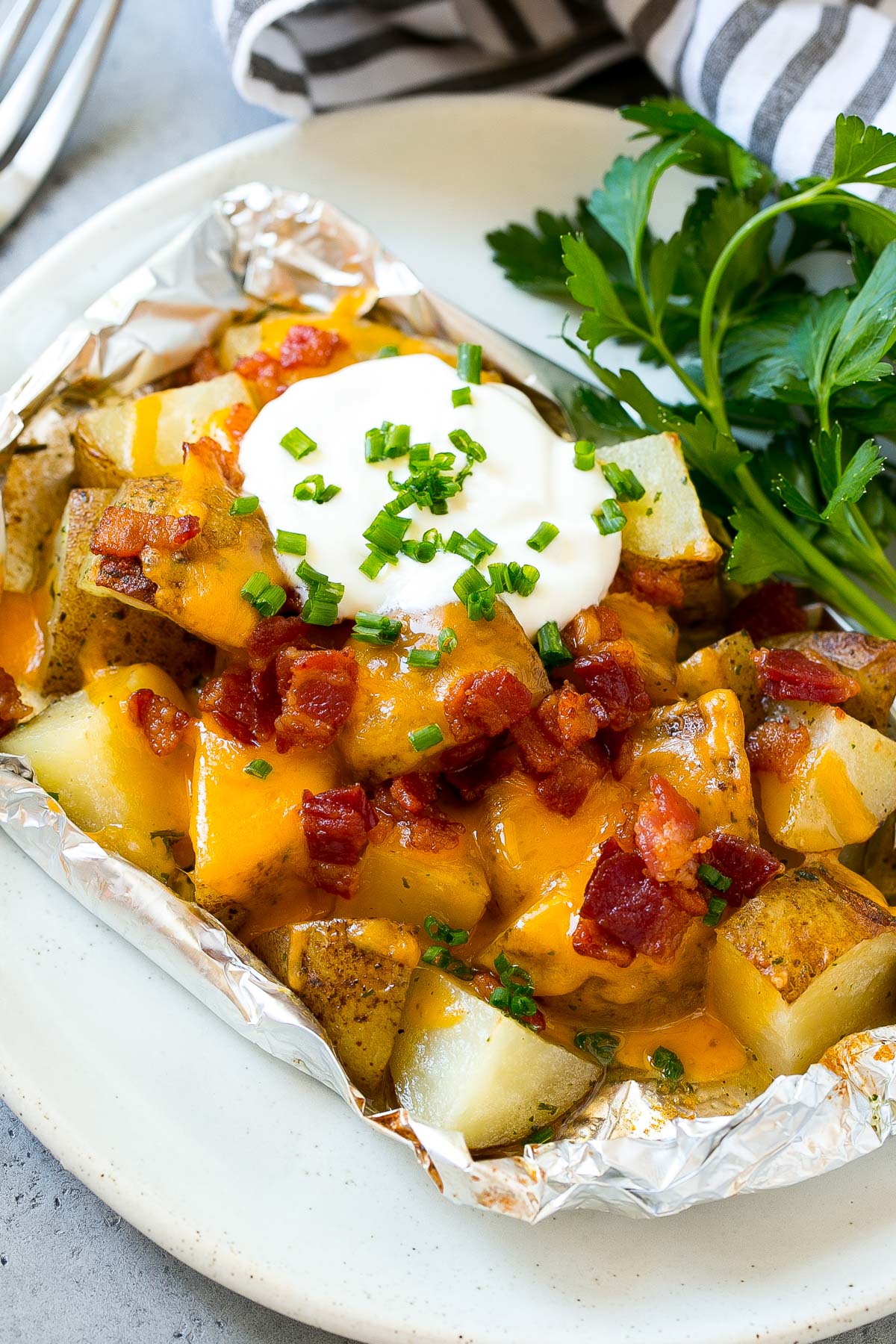 Grilled potatoes in foil on a serving plate garnished with herbs.