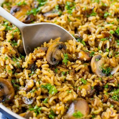 A skillet of easy mushroom rice with a serving spoon in it.