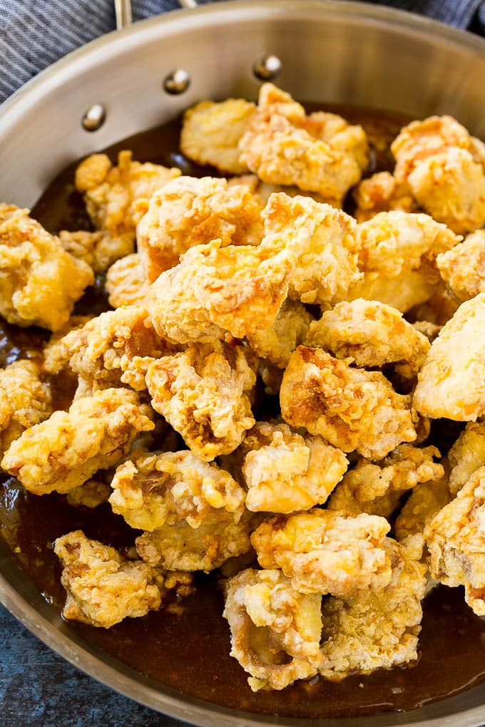 Crispy chicken pieces in a pan of orange sauce.