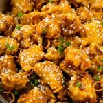 Orange chicken in a skillet with crispy chicken, sesame seeds, orange zest and green onions.