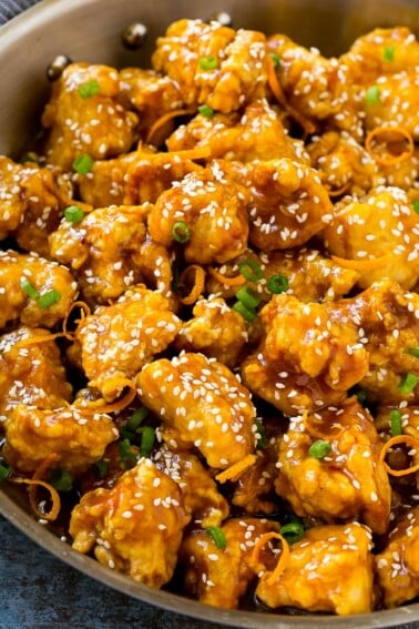 Orange chicken in a skillet with crispy chicken, sesame seeds, orange zest and green onions.