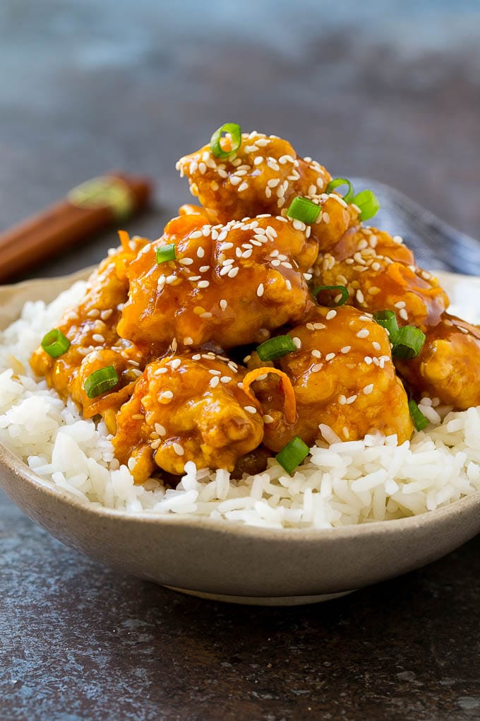 A bowl of orange chicken served over steamed rice and topped with sesame seeds.