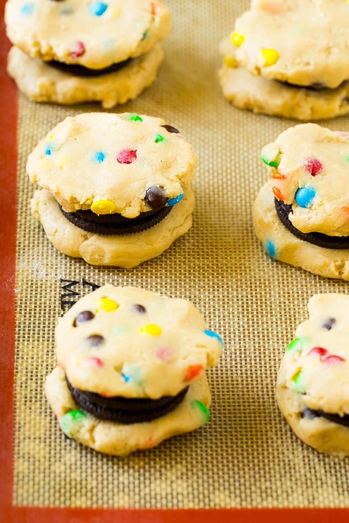 Oreo Stuffed Cookies Recipe | M&M's cookies | Stuffed Cookies #cookies #chocolate #oreos #dessert #baking #dinneratthezoo Cookie dough sandwiched around Oreos on a baking sheet.