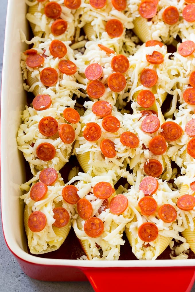 Pasta shells topped with mini pepperoni and shredded cheese in a baking dish.