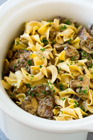 Slow cooker beef stroganoff with chunks of beef, mushrooms and egg noodles topped with parsley.