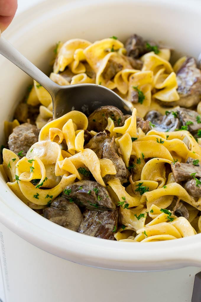 A crock pot of beef stroganoff with a serving spoon in it.