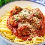 Slow cooker meatballs served over spaghetti, topped with parsley and parmesan cheese.