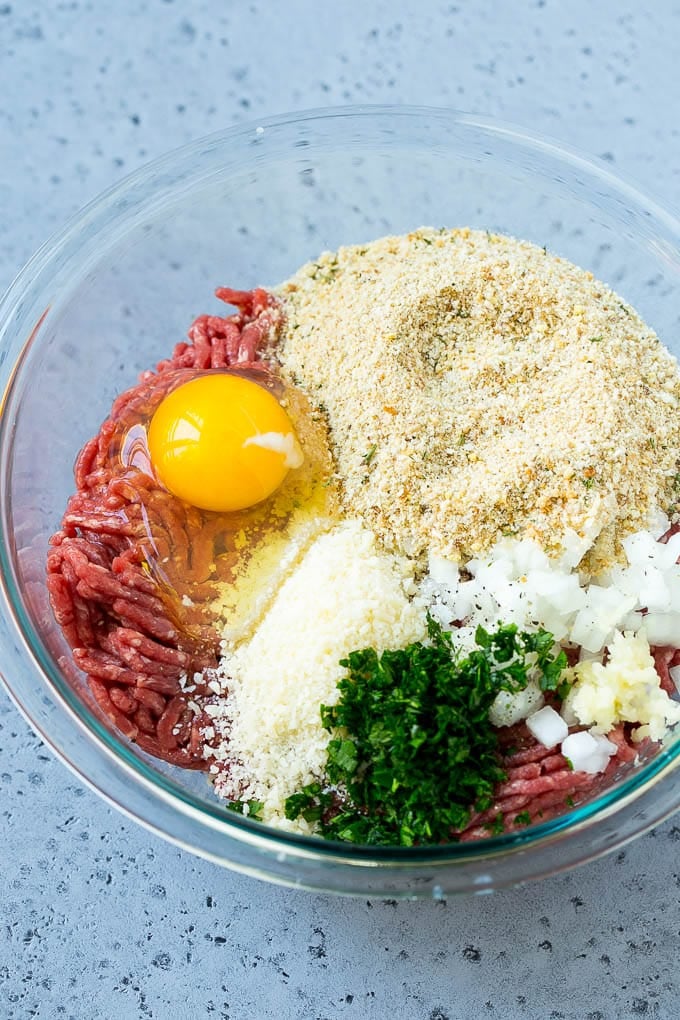 Ground beef, onion, garlic, herbs, cheese and breadcrumbs in a mixing bowl.