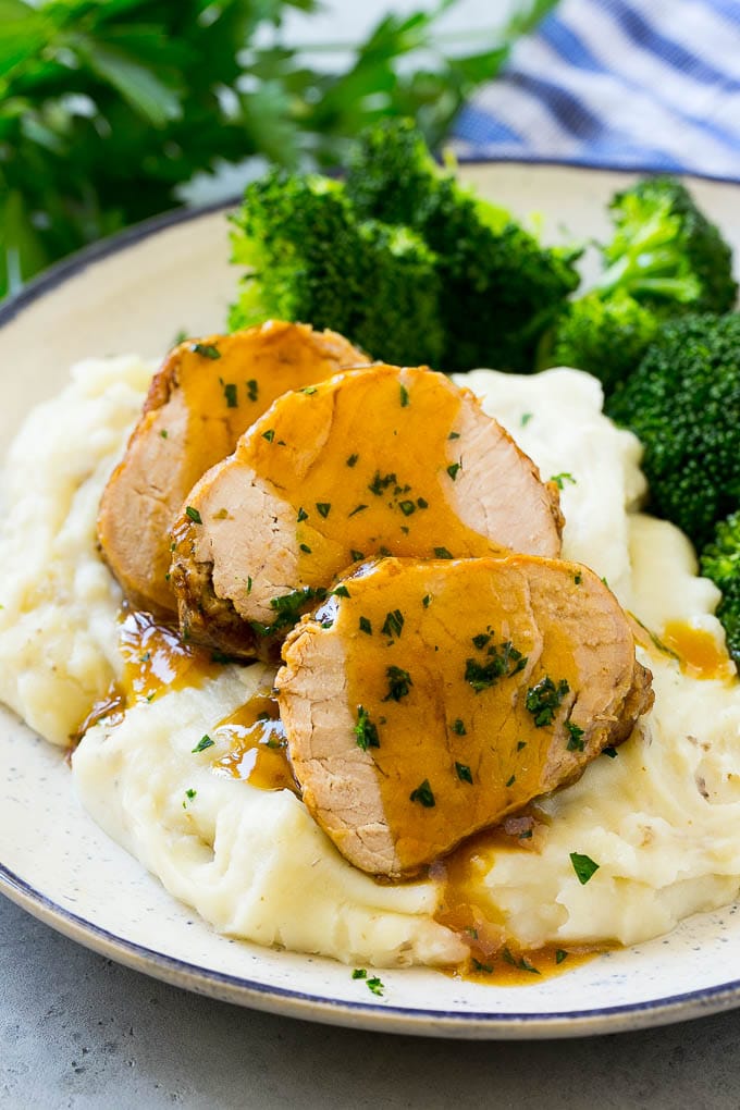 Sliced slow cooker pork tenderloin served over mashed potatoes with broccoli.