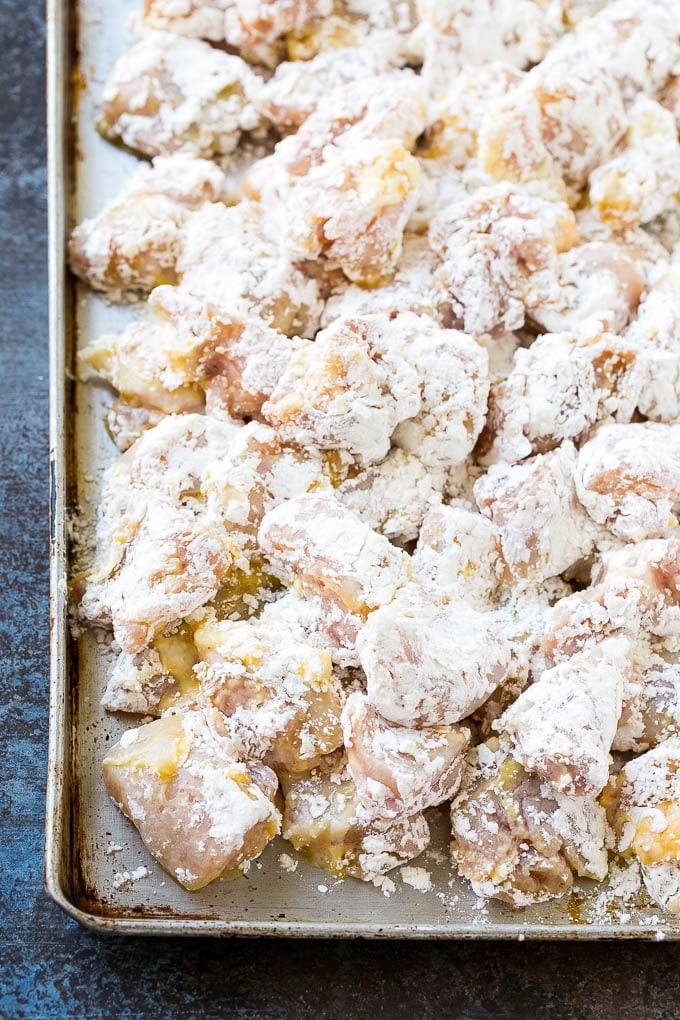 Chicken pieces coated in egg and flour on a baking sheet.