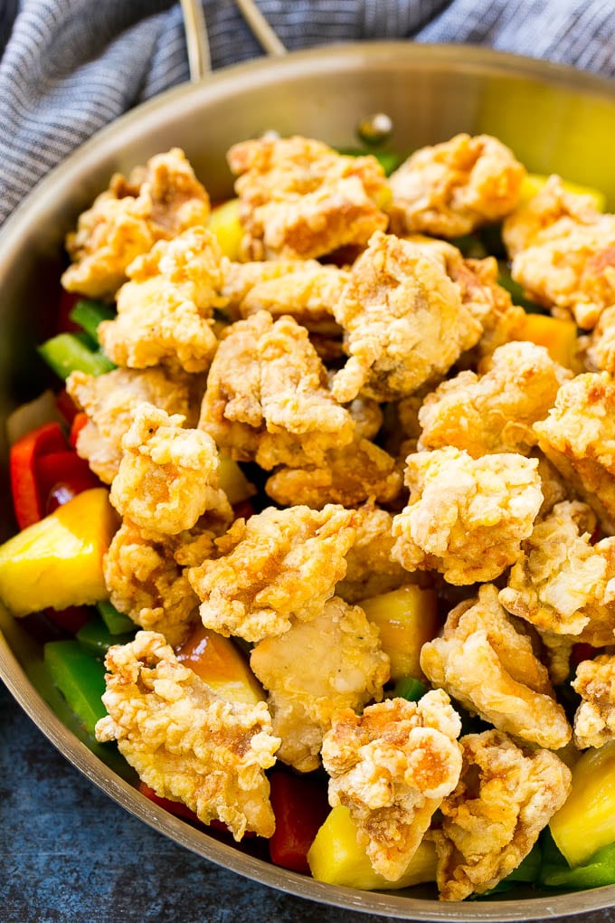 Fried chicken pieces in a pan with pineapple, peppers and onions.