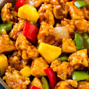 A frying pan of sweet and sour chicken with crispy chicken, pineapple, bell peppers and onions.