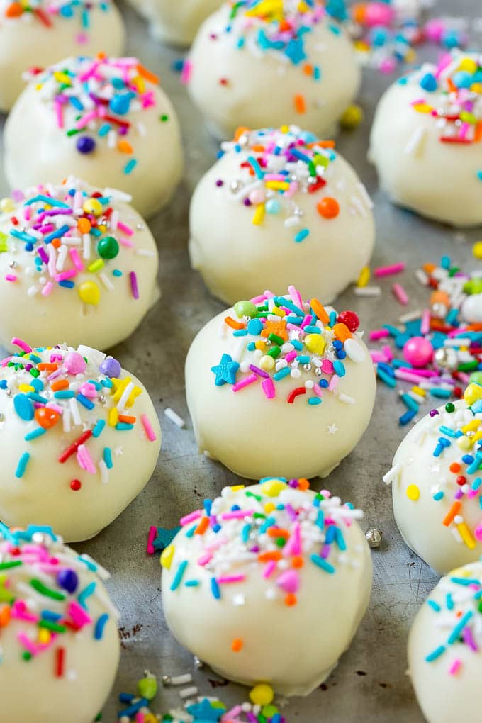 Cake balls coated in white chocolate and sprinkles on a sheet pan.