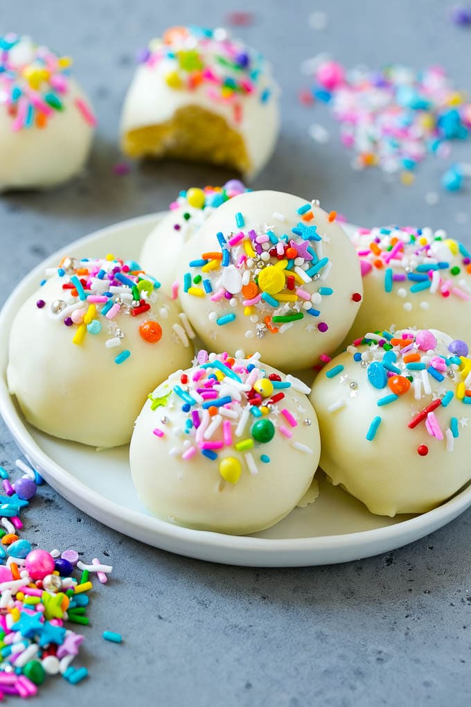 A plate of cake balls coated in white chocolate and rainbow sprinkles.