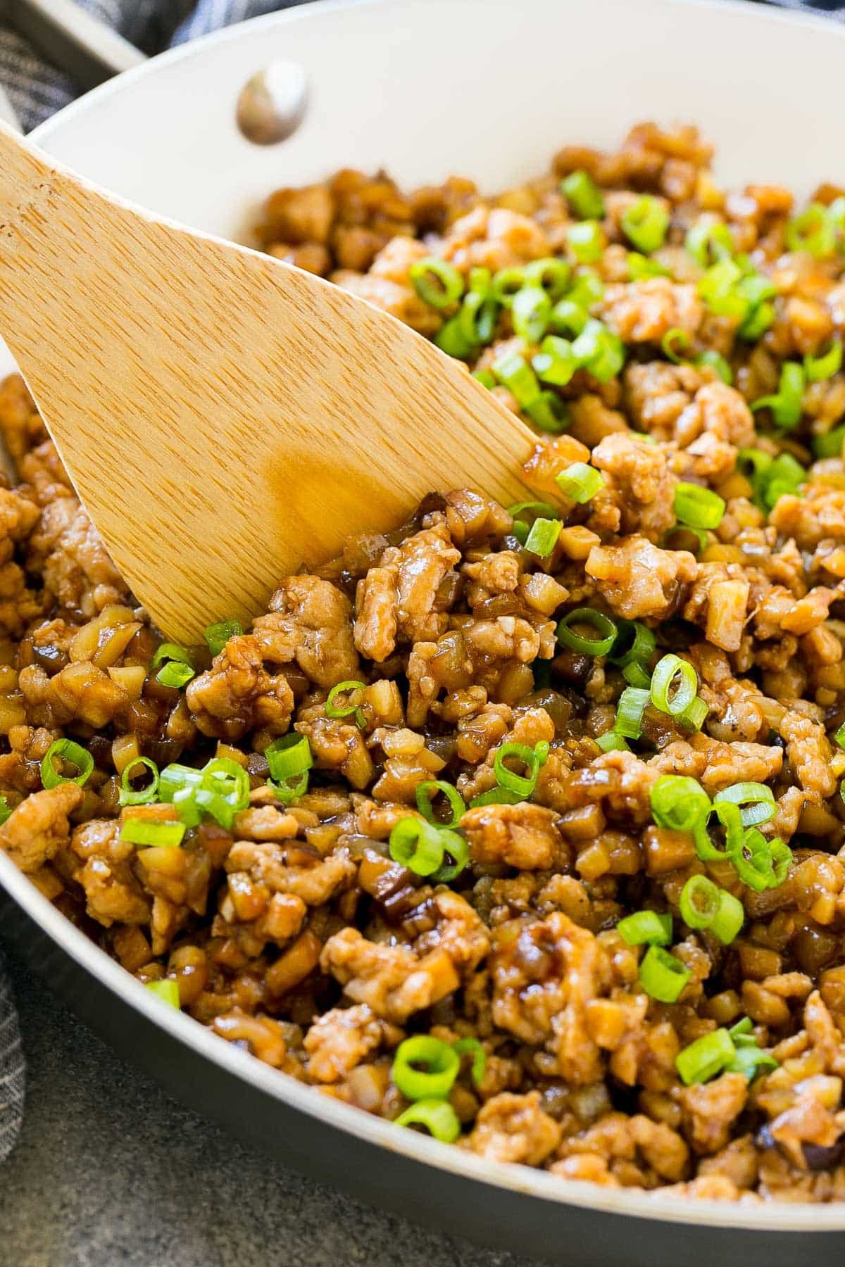Ground chicken in a pan with sauce and green onions.