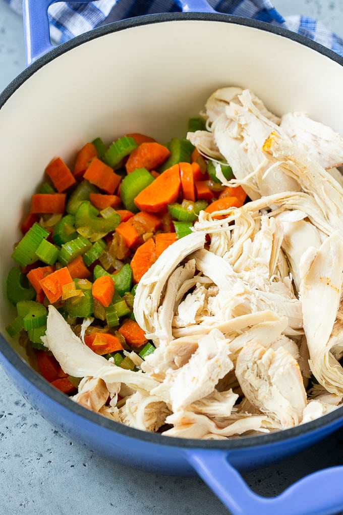 A soup pot full of sauteed vegetables and shredded chicken.