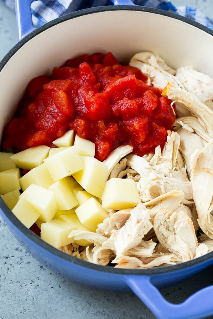 Chiccken, vegetables, potatoes and tomatoes in a soup pot.