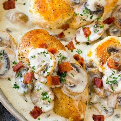 A skillet of mushroom chicken in a creamy sauce, topped with bacon and herbs.