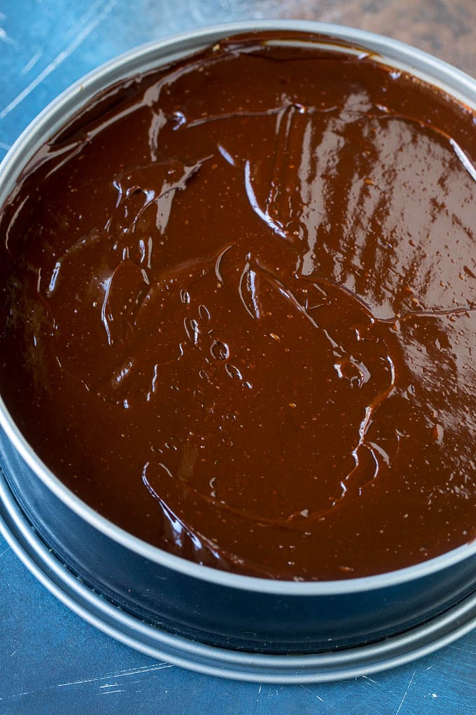 A layer of chocolate ganache on top of an Oreo cheesecake.